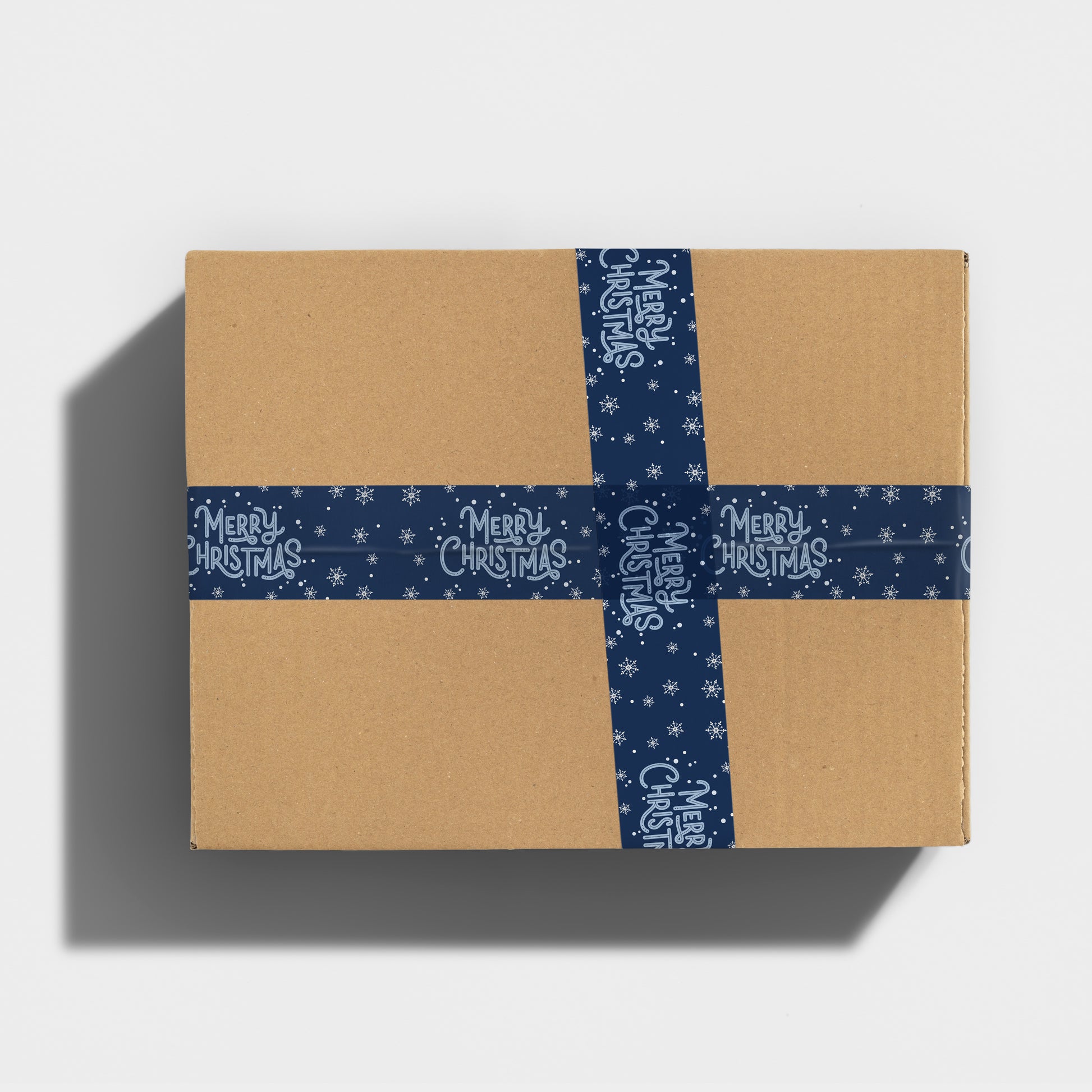 Holiday gift box secured with festive Merry Christmas printed tape on a snowy navy blue background.