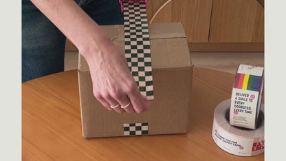 A woman is applying a strong and durable checkerboard pattern packing tape to a box.